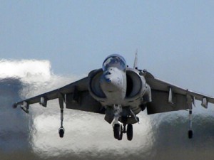 An AV-8B Harrier II Jet landing vertically onto the tarmac.