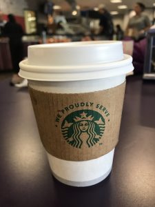 This image shows a cup that has he Starbucks logo on the sleeve that says, “We proudly serve” above the mermaid logo. Photo taken by The Signal reporter Marielle Gomez.