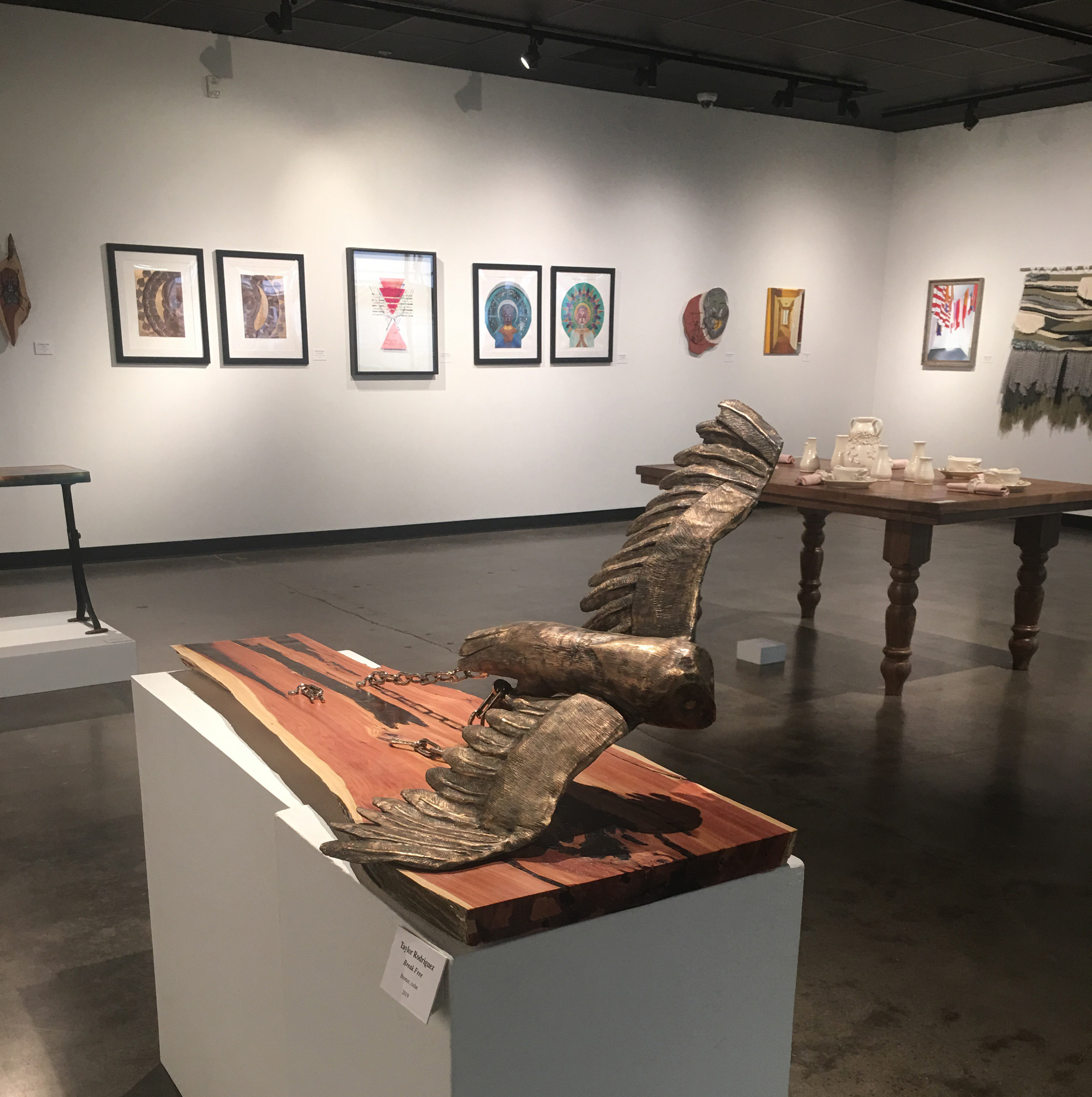 PHOTO: This years BFA show was the first to utilize the additional space of the new wing. With artwork held in both wings large works like Taylor Rodriguez's "Break Free" and McKenna Bailey's "Handmade" could center the rooms. Image is of main wing with Rodriguez's "Break Free" cedar and bronze owl sculpture in the center. Behind is Bailey's "Handmade," a hand made table and table setting with ceramics. Photo by The Signal Online Editor Alyssa Shotwell.